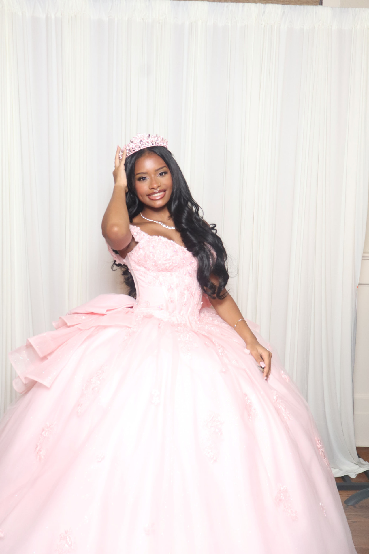 A guest in a pink ball gown and tiara smiling in front of an ivory drape