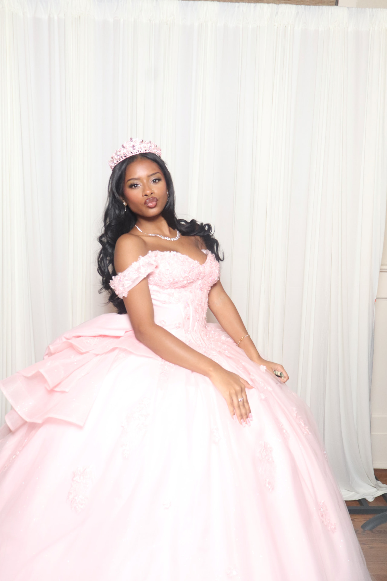 A guest in a pink ball gown and tiara posing in front of an ivory drape